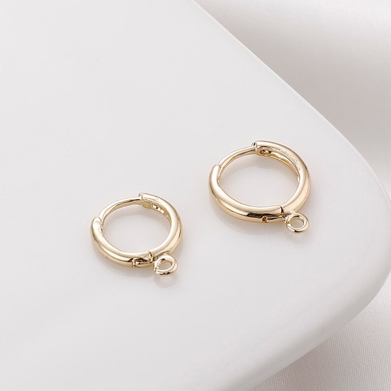 May include: Two gold hoop earrings with a small loop hanging from the bottom of each hoop.