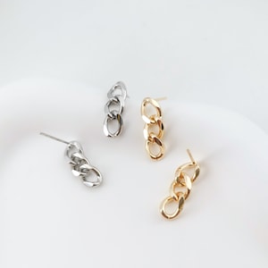 Puede incluir: Dos pares de pendientes de eslabones de cadena, un par es dorado y el otro es plateado.