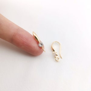 May include: Two gold earring hooks with clear crystal accents. The hooks are designed to be used for hanging earrings.