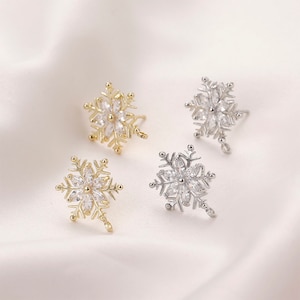 May include: Three snowflake earrings with clear crystal accents. Two earrings are silver and one is gold.