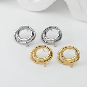 Peut inclure: Quatre paires de boucles d'oreilles argentées et dorées. Chaque boucle d'oreille présente un design à double boucle avec une petite boucle en bas pour attacher des breloques. Les boucles d'oreilles sont présentées sur une surface blanche.