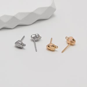Puede incluir: Tres pendientes de botón en tonos plateados y dorados. Los pendientes tienen un diseño texturizado e irregular, que se asemeja a pequeñas piedras. Los postes son finos y los pendientes se muestran sobre una superficie blanca.