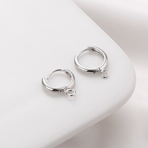 May include: Two silver hoop earrings with a small jump ring attached to the bottom of each hoop.