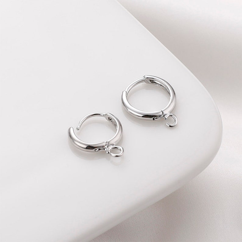May include: Two silver hoop earrings with a small jump ring attached to the bottom of each hoop.