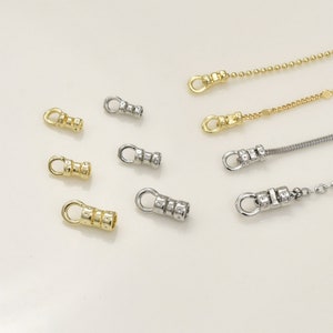 Peut inclure: Un ensemble de fermoirs de chaîne en métal doré et argenté. Les fermoirs ont une petite boucle en haut et un corps cylindrique avec un motif texturé.