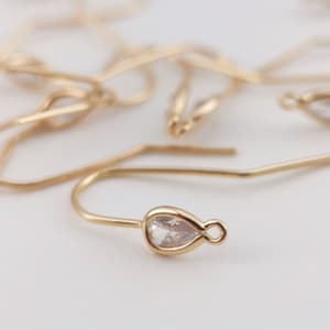 Puede incluir: Ganchos de pendientes de tono dorado con un cristal transparente en forma de l&aacute;grima.