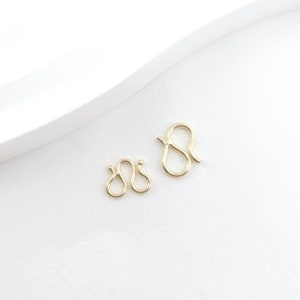 May include: Two gold-toned metal lobster clasps, one larger than the other, on a white background.
