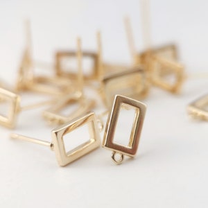 May include: Gold-toned earring blanks with a rectangular frame. The earring blanks have a post and a loop on the bottom.