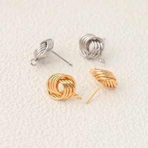 May include: Two pairs of stud earrings featuring a circular knot design. One pair is finished in a bright silver tone, while the other pair is finished in a polished gold tone. Each earring consists of multiple thin metal loops intertwined.