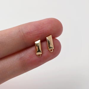 May include: Two small, rectangular gold-colored jewelry findings. Each finding has a loop at the bottom and a slightly angled top. The findings are displayed against a white background.