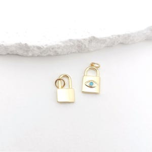 May include: Two gold lock charms, one with a blue evil eye design. The charms are on a white background.