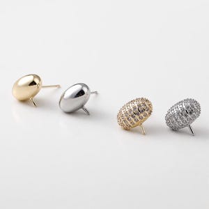 Pode incluir: Quatro pares de brincos de pressão em ouro, prata e cristal. Dois pares têm um design oval liso, enquanto os outros dois são cobertos por pequenos cristais. Os brincos são exibidos em uma superfície branca.