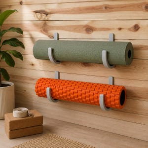May include: A wall-mounted storage system featuring two sets of light gray U-shaped brackets. The top bracket holds a rolled olive green yoga mat, while the bottom bracket supports a bright orange textured foam roller for exercise routines.