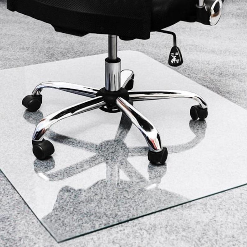 May include: A clear, rectangular floor mat made of rigid material placed underneath a black office chair. The chair features a chrome-finished five-point base with black plastic casters and a height adjustment lever with a white icon.