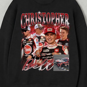 May include: Black crewneck sweatshirt featuring a vintage-style graphic of Christopher Bell, a race car driver. The design includes a portrait of Bell and other racers, with the name "Christopher" and "Bell" in red and white lettering.