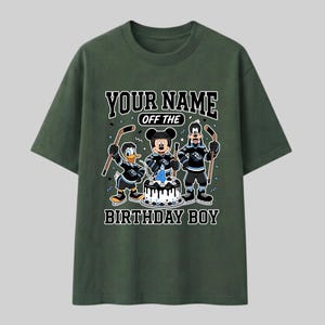 May include: Dark green t-shirt with a cartoon graphic of Mickey Mouse, Donald Duck, and Goofy in hockey attire. The shirt displays the text "YOUR NAME OFF THE BIRTHDAY BOY". A birthday cake with the number 4 is in the center of the design.