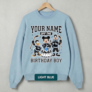 May include: Pale blue sweatshirt with a cartoon hockey-themed design. It features Mickey Mouse, Donald Duck, and Goofy, plus the text "YOUR NAME OFF THE BIRTHDAY BOY" and a cake with a number 4 candle. The bottom of the sweatshirt says "LIGHT BLUE".
