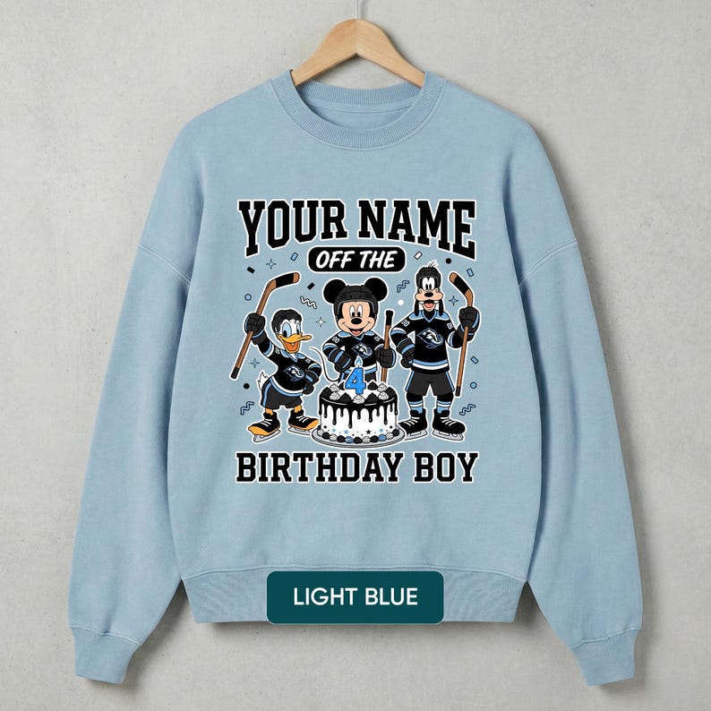 May include: Pale blue sweatshirt with a cartoon hockey-themed design. It features Mickey Mouse, Donald Duck, and Goofy, plus the text "YOUR NAME OFF THE BIRTHDAY BOY" and a cake with a number 4 candle. The bottom of the sweatshirt says "LIGHT BLUE".