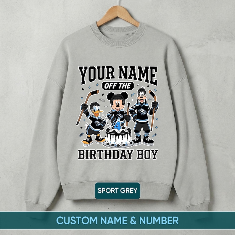 May include: Grey sweatshirt with a hockey-themed birthday design. It features cartoon characters, a birthday cake with a number 4 candle, and the text "YOUR NAME OFF THE BIRTHDAY BOY".