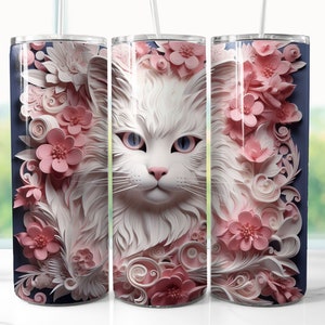 Puede incluir: Gato blanco con flores rosas y diseños intrincados de papel sobre un fondo azul. La cara del gato está centrada y las flores están a ambos lados de la cara del gato. Este es un diseño para un vaso.