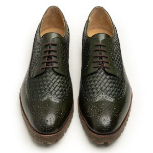 May include: A pair of dark green leather dress shoes with woven detailing on the toe and sides. The shoes have brown laces and soles, and a classic brogue design with decorative perforations.