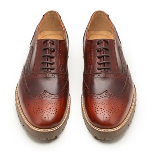 Peut inclure: Une paire de chaussures brogues en cuir marron avec un design à bout d'aile. Les chaussures ont une fermeture à lacets classique et une semelle épaisse marron clair. Le cuir a une finition polie et des perforations décoratives.