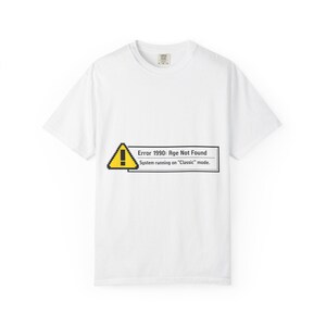 May include: White t-shirt with a graphic that resembles a computer error message. The message reads "Error 1990: Age Not Found" with a yellow warning sign and the text "System running on 'Classic' mode."