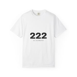 May include: White t-shirt with the number "222" and the word "ALIGNMENT" printed in black. The shirt has a crew neck and short sleeves. The fabric appears to be a soft cotton blend.