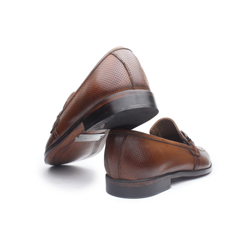 May include: A pair of brown leather loafers featuring a micro-perforated texture across the upper surface, a dark brown stacked heel, and a dark brown sole. The shoes are positioned with one resting on its side to reveal the bottom sole detail.