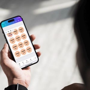 May include: A smartphone screen displaying a digital template for creating personalized labels. The template features a grid of 16 circular labels with the text "NAME" and "DATE" on each label. The labels are peach-colored with black text.