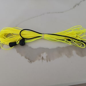 May include: A coiled yellow rope with a black handle and a black clip. The rope is tied together with a white zip tie. Two black stoppers are attached to the yellow rope.