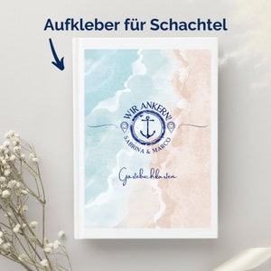 May include: A white guest book with a beach-themed design. The cover features a watercolor illustration of a beach scene in shades of blue and tan, with an anchor and the words "Wir Ankern!" and "Sabrina & Marco". The words "Guestbook Cards" are also visible.