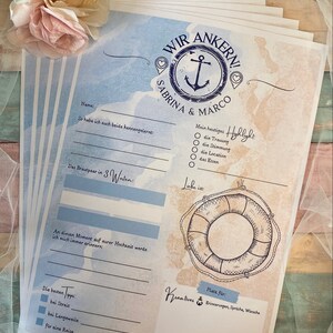 May include: A stack of wedding stationery with a nautical theme. The design features an anchor, the names "Sabrina & Marco", and fill-in-the-blank prompts. The color scheme includes blue, beige, and white, with a decorative floral accent.