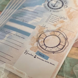 May include: A nautical-themed wedding guest book with blue and beige watercolor backgrounds. The design includes an anchor, a life preserver illustration, and text in German. The book has space for memories, wishes, and quotes.