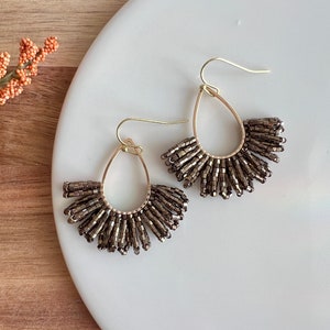 May include: A pair of gold hoop earrings with a teardrop shape. The hoops are adorned with brown beads that hang down in a fan shape.