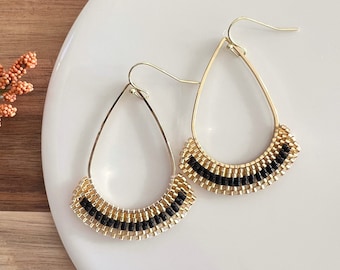 May include: A pair of gold teardrop earrings with black and gold beaded detailing.