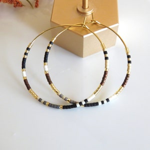 May include: A pair of gold hoop earrings with brown, black, white, and gray beads.