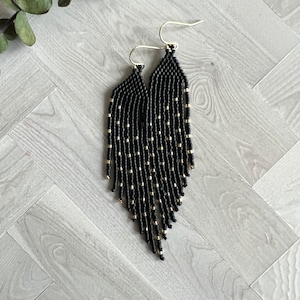 May include: Black and gold beaded earrings with a fringe design. The earrings are long and dangle.