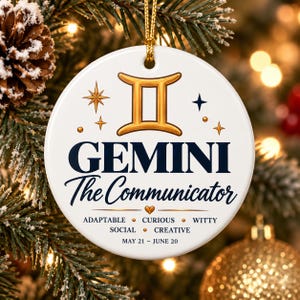 Op de afbeelding: Een ronde witte keramische hanger met het gouden sterrenbeeldteken Tweelingen, de tekst GEMINI The Communicator, de woorden ADAPTABLE, CURIOUS, WITTY, SOCIAL, CREATIVE, en de data MAY 21 - JUNE 20, opgehangen aan een gouden koord.