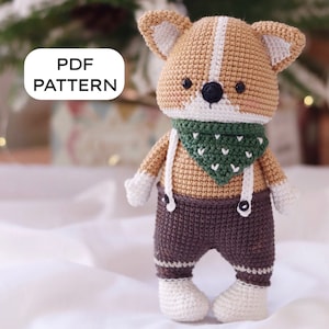 Puede incluir: Patrón de crochet para un adorable zorro amigurumi marrón y blanco que lleva un pañuelo verde y pantalones marrones con tirantes blancos. El patrón está disponible para descargar en PDF.