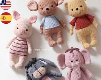 May include: Five crocheted stuffed animals: a brown bear wearing a blue shirt, a yellow bear wearing a red shirt, a pink pig wearing a striped shirt, a gray donkey, and a pink elephant. The animals are all standing on a white surface. The image includes the text "@luluptitedoll".