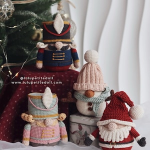 Può includere: Ornamenti natalizi fatti a mano all'uncinetto, tra cui uno schiaccianoci, un pupazzo di neve e Babbo Natale. Gli ornamenti sono in vari colori, come blu, rosa, rosso e bianco. L'indirizzo del sito web è visibile.