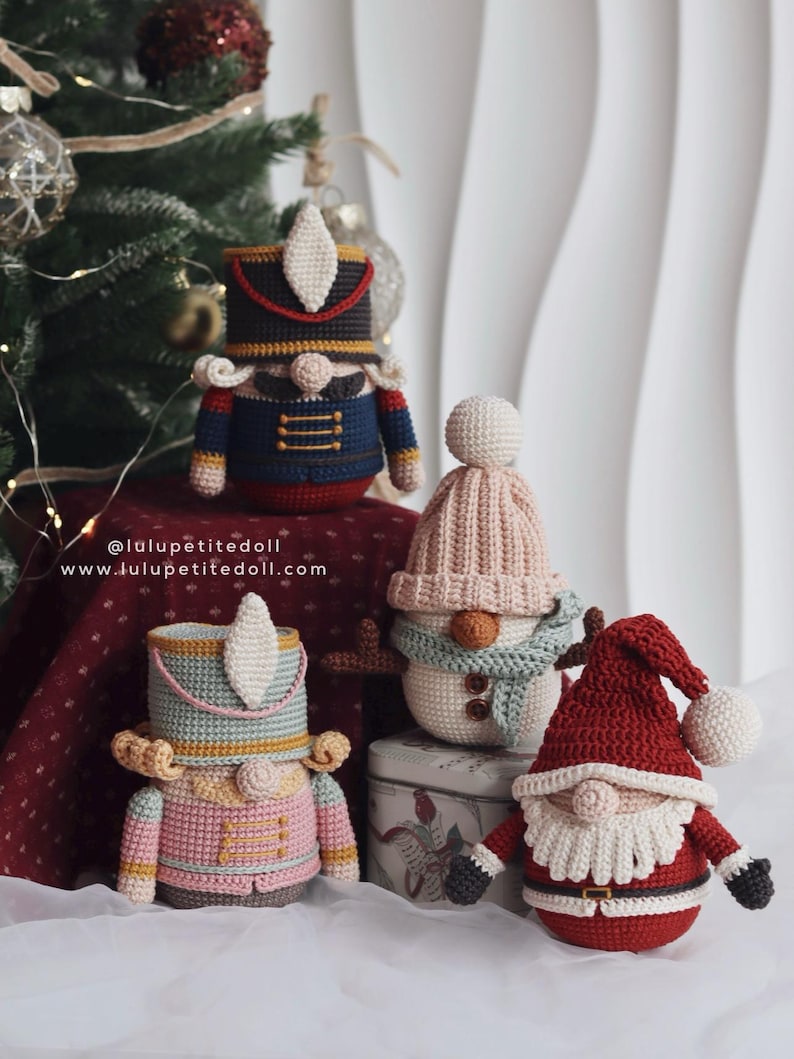 May include: A collection of handmade crochet Christmas ornaments, including a nutcracker, snowman, and Santa Claus. The ornaments are in various colors, such as blue, pink, red, and white. The website address is visible in the image.