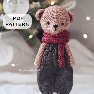 May include: A crocheted teddy bear wearing a brown jumpsuit and a red scarf. The bear has a brown nose and black eyes. The bear is standing on a white surface. The text "PDF PATTERN" is in a white rectangle on the left side of the image. The text "@luluptitedoll" is below the bear.