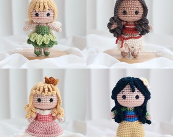 May include: Four crocheted dolls, each representing a different Disney princess. The dolls are standing on a white surface. The princesses are: Tinkerbell, Moana, Aurora, and Mulan.
