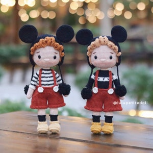 Może przedstawiać: Dwie szydełkowe lalki z uszami Myszki Miki, ubrani w czarno-białe pasiastych koszule, czerwone ogrodniczki i czarne skarpetki. Lalki mają brązowe włosy i stoją na drewnianej powierzchni.