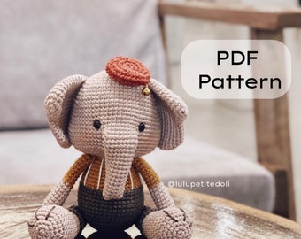 May include: Crochet pattern PDF for a cute gray elephant amigurumi toy with a red hat, brown eyes, and a yellow and brown striped shirt. The pattern is available for download from @lulupettitedoll.