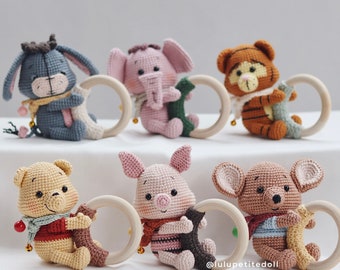 May include: Six crocheted stuffed animal toys with wooden rings. The toys include a donkey, elephant, tiger, bear, pig, and a brown animal with large ears. The toys are all wearing scarves and are holding the wooden rings.