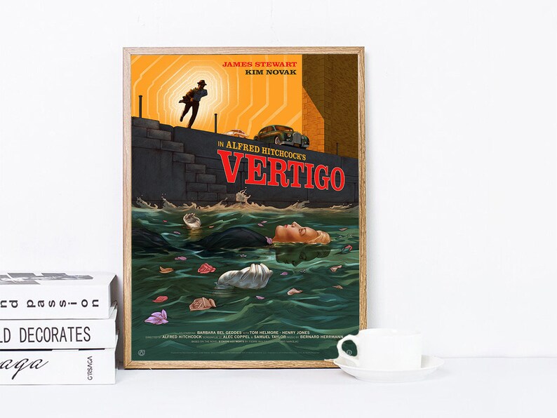 May include: A framed movie poster for Alfred Hitchcock's "Vertigo." The artwork features a man running, a woman in the water, and the title in red. The poster has a vintage aesthetic with a wooden frame.