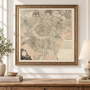 May include: A framed antique map of a city, featuring intricate street layouts, river paths, and green spaces in muted tones of beige, tan, and soft green. The map is enclosed in a textured, dark gold-toned wooden frame with a decorative border.